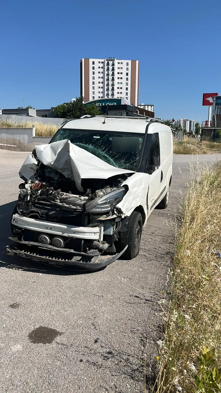 Ön kaportası, motor bölümü ve tamponu tamamen parçalanmış beyaz Fiat Doblo panelvan, yol kenarında.